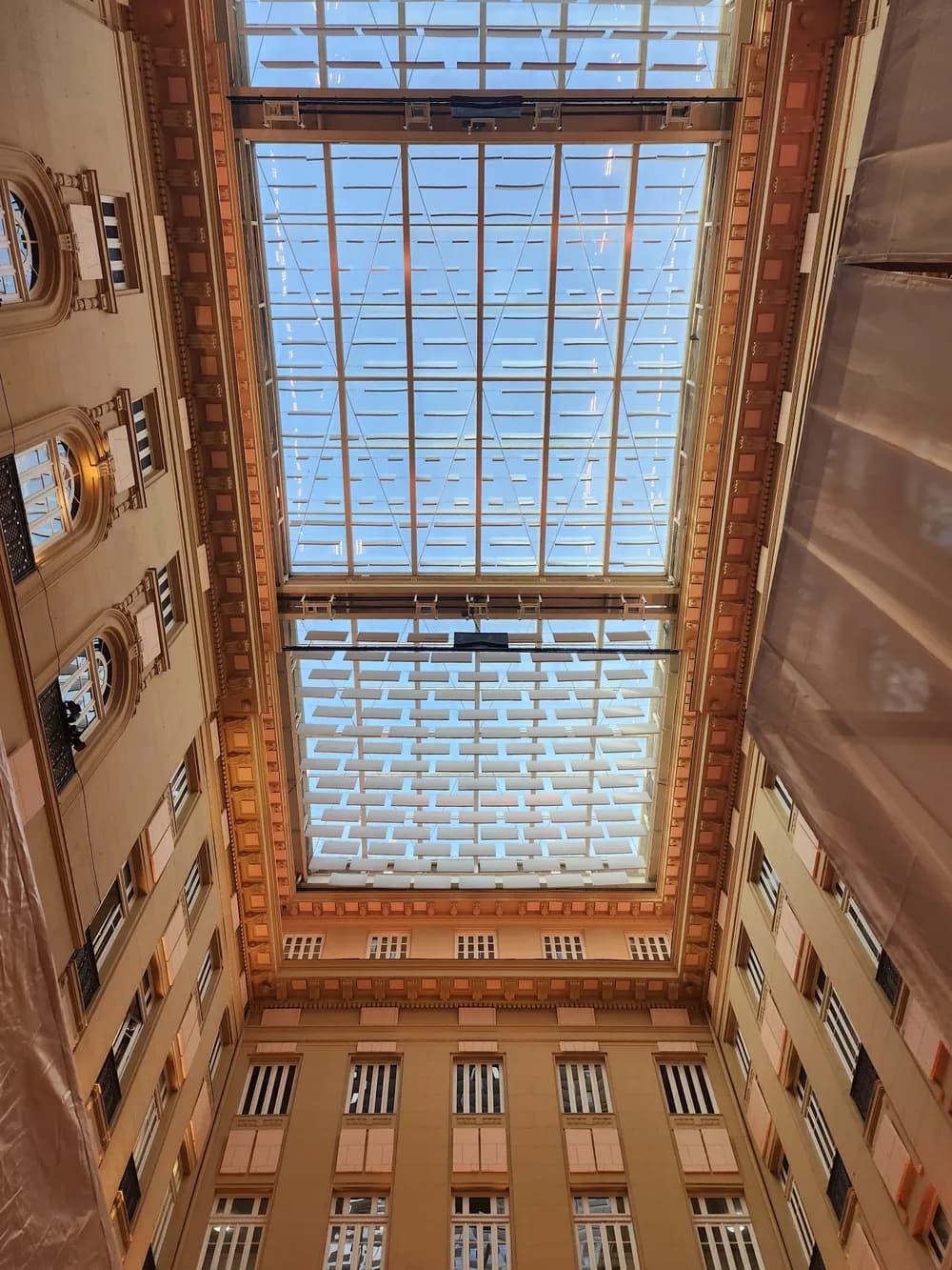 Looking straight up a warm-toned courtyard to a glass skylight hung with rows of white panels.